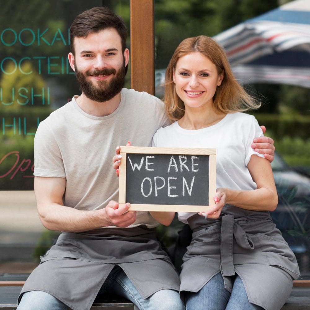 A couple getting started with a local SEO holds a sign that says we are open.